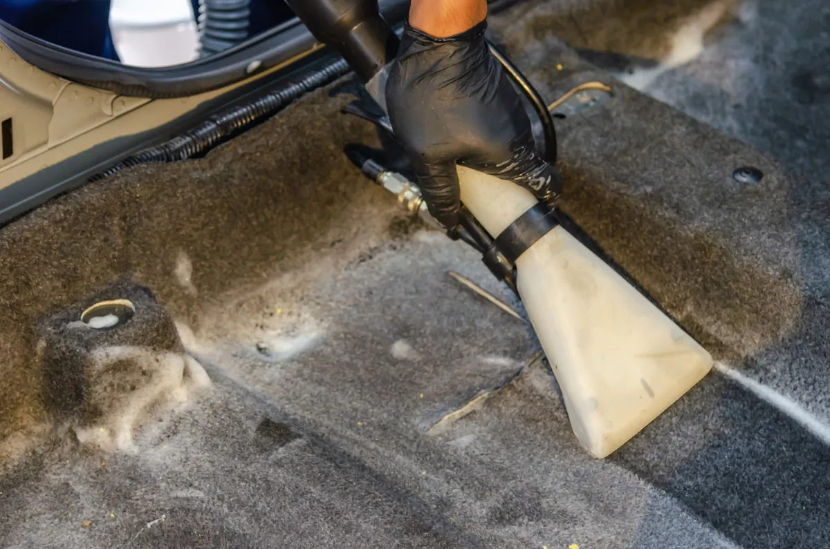 A gloved hand pulling dirt from car carpet with an extractor