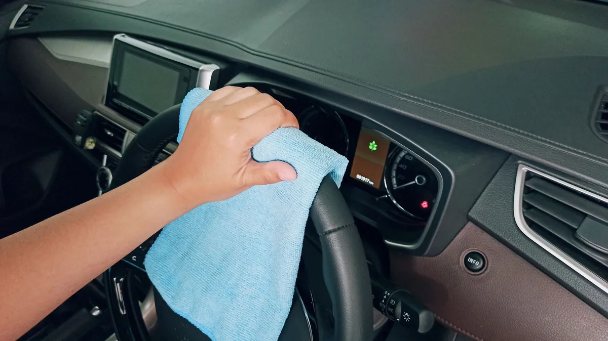 A blue microfiber cloth wiping the dashboard behind the steering wheel