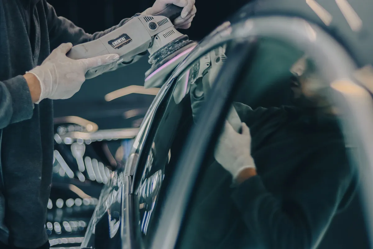 Gloved hands finishing the paint on a dark car