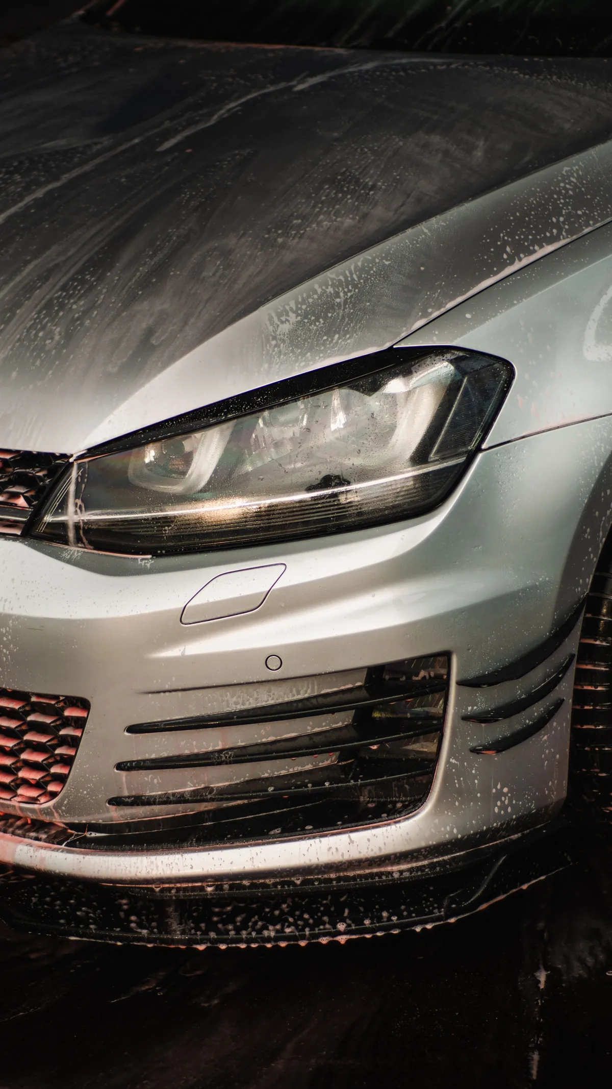 Water beading on a silver hatchback's headlight and hood