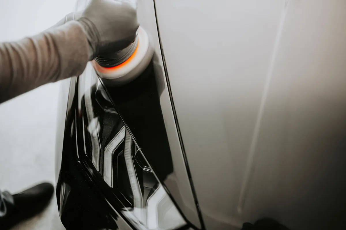 A gloved hand running a polisher across a black panel