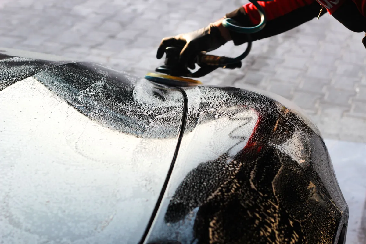A dual-action polisher working across a dark fender