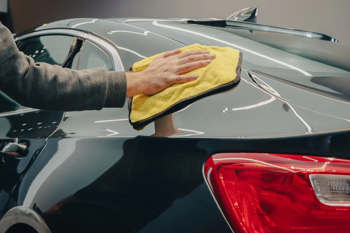 A yellow microfiber towel wiping a dark green car above the taillight