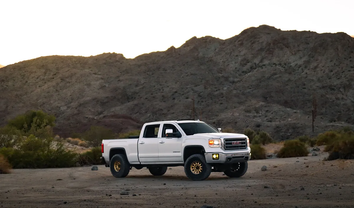 A clean white pickup parked on desert gravel below dry mountains